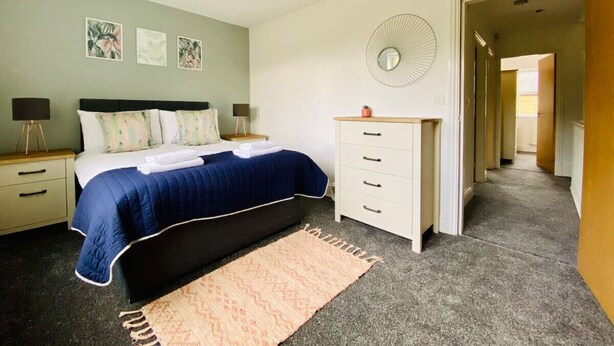 Une chambre à coucher comprenant un lit, des tables de chevet, une commode, un miroir et un ventilateur.