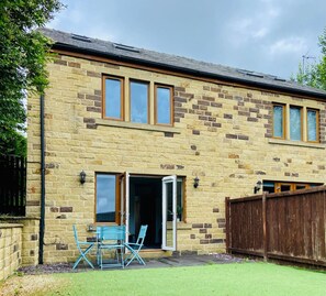 A two-story stone building with a patio area, a wooden fence, and a door leading to an interior space.