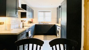 Une cuisine de taille réduite, dotée de meubles de couleur sombre, d’un îlot central et d’une fenêtre qui laisse entrer la lumière naturelle.