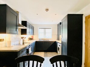 A compact kitchen with dark cabinets, a central island, and a window providing natural light. - Garden+Pets OK |8mins Halifax |Parking |M62 Access (Halifax)