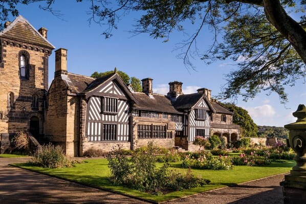 Traditional Tudor-style building with a symmetrical facade, arched windows, and a pitched roof, set amidst a well-manicured garden.