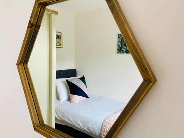 A room with a bed, a headboard, and a mirror with a geometric frame.