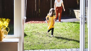 Un enfant vêtu d’un t-shirt jaune joue dans un jardin, avec une clôture en bois et un parterre de fleurs en arrière-plan.