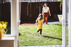 A child in a yellow shirt playing in a backyard with a wooden fence and a garden bed in the background.
