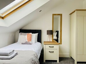 Ein Schlafzimmer mit Bett, Nachttisch, Lampe, Spiegel und Kleiderschrank.