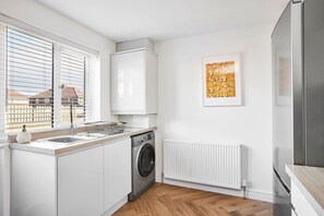 Cocina moderna con armarios blancos, lavadora integrada, refrigerador de acero inoxidable y una ventana con persianas.