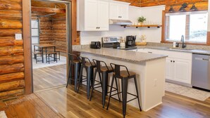 A log cabin-style kitchen with white cabinets, a granite countertop, and bar stools.
