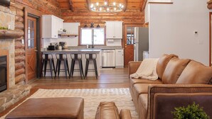 A log cabin interior with a kitchen, living area, and a fireplace.