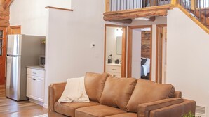 A spacious living room with a brown leather sofa, a white rug, and a wooden ceiling with exposed beams.