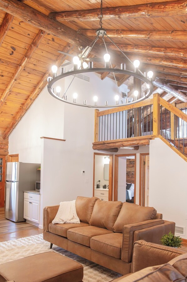 A spacious living room with a brown leather sofa, a white rug, and a wooden ceiling with exposed beams.