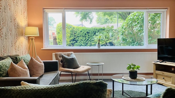 Una sala de estar con sofá, sillón, una mesita redonda y un mueble para televisión.