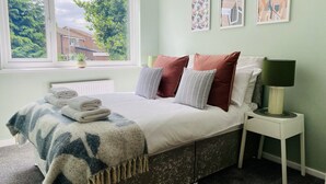 Un dormitorio con cama, ventana, mesita de noche y una obra de arte en la pared.