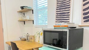 Pieni ja käytännöllinen keittiö, jossa on turkoosinsininen jääkaappi, sen päälle sijoitettu mikroaaltouuni, puinen pöytä ja tuoli.
