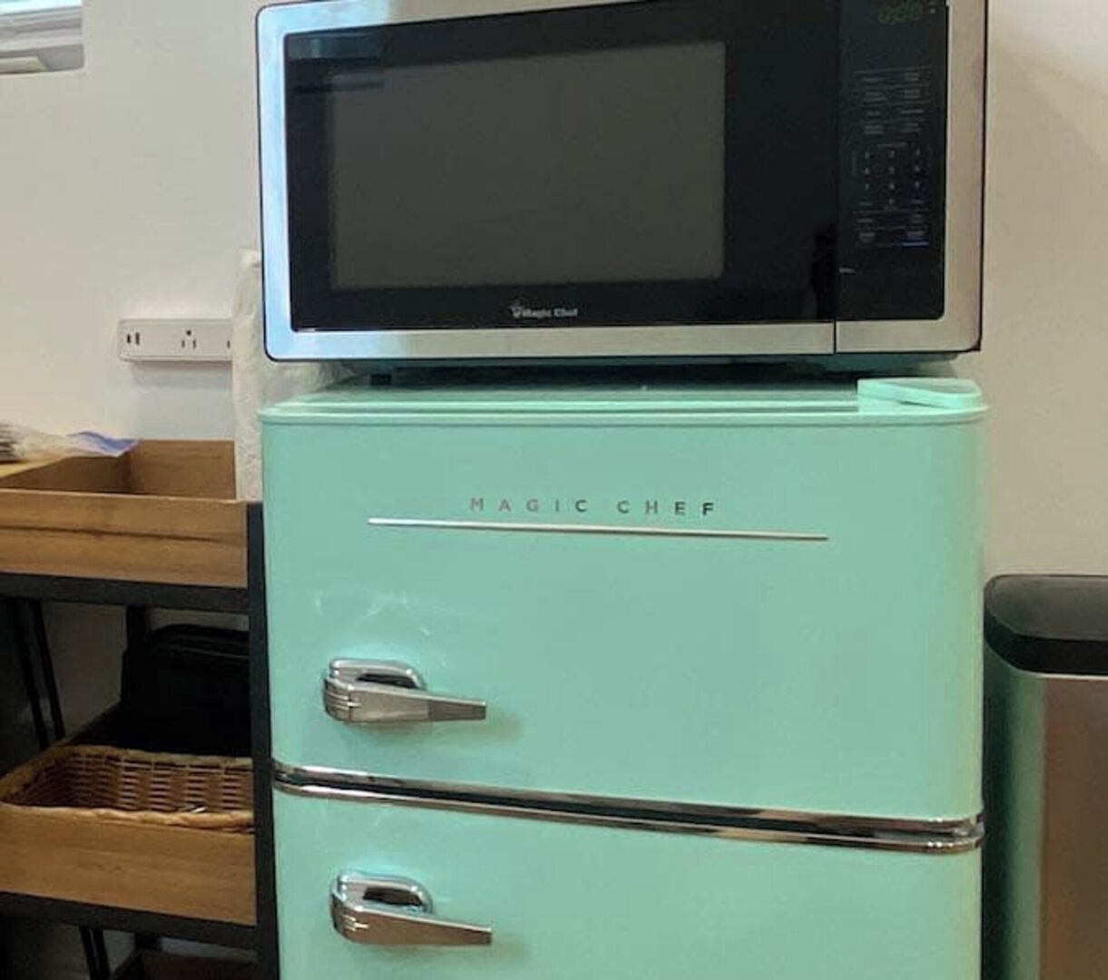 Un réfrigérateur de couleur turquoise avec un four à micro-ondes placé sur le dessus, portant l’inscription « Magic Chef ».