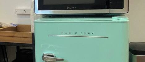 Un réfrigérateur de couleur turquoise avec un four à micro-ondes placé sur le dessus, portant l’inscription « Magic Chef ».