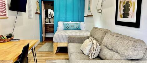 A compact living space with a bed, a sofa, a dining table, and a TV.