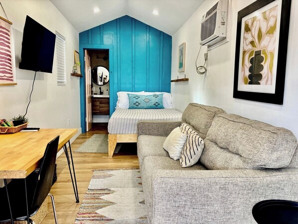 Un espacio habitable compacto con cama, sofá, mesa de comedor y televisor.