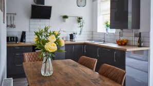 Une cuisine moderne avec des meubles de couleur sombre, une table à manger en bois et un vase rempli de fleurs.
