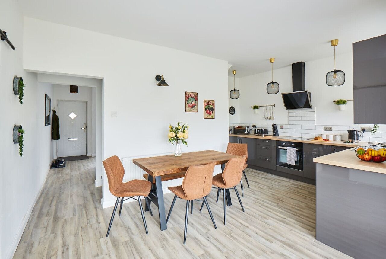 Une cuisine moderne avec une table à manger en bois, quatre chaises et des luminaires suspendus.