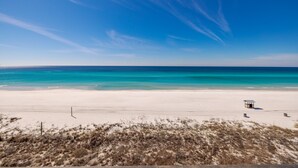 Una playa con cielo despejado, orilla arenosa y una estructura pequeña a lo lejos.
