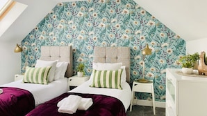 Une chambre avec deux lits, un plafond en pente et un papier peint à motifs floraux.