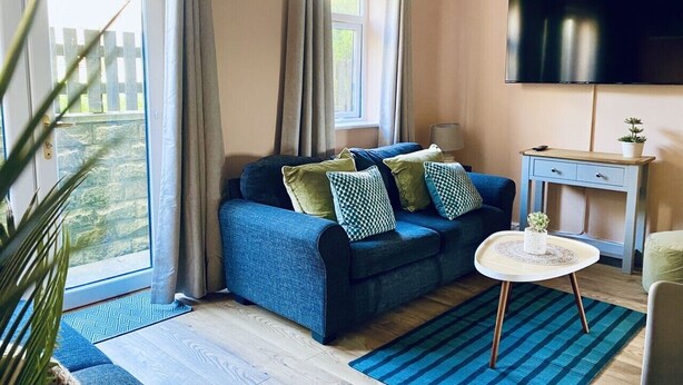 Un salon avec un canapé bleu, une petite table ronde, un téléviseur et une fenêtre avec des rideaux.