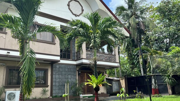 A two-story house with a balcony, surrounded by lush greenery and palm trees. - Dovilim Apartments (Tacloban)