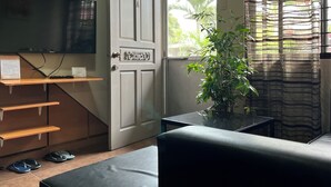 A room with a television mounted on the wall, a door with a decorative handle, a potted plant, and a window with curtains. - Dovilim Apartments (Tacloban)