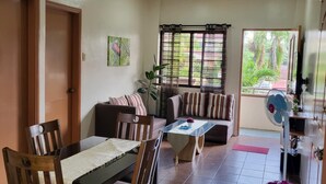 A dining area with a table and chairs, a sofa, and a fan. - Dovilim Apartments (Tacloban)