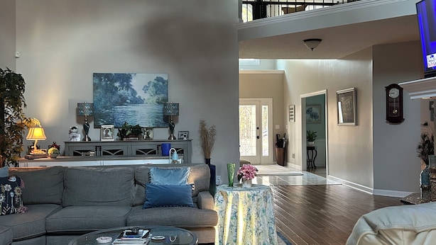 A spacious living room with a large sectional sofa, a glass coffee table, and a ceiling fan. A painting is on the wall, and there is a staircase leading to an upper level. - Charming spacious home nestled on a private lot minutes away from the Masters (Augusta)