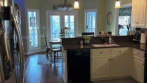 A kitchen with wooden flooring, white cabinets, a dishwasher, and a refrigerator. - Charming spacious home nestled on a private lot minutes away from the Masters (Augusta)