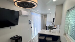Ein modernes Wohnzimmer mit Flachbildfernseher, Wasserspender, Deckenventilator und einer Sitzecke.