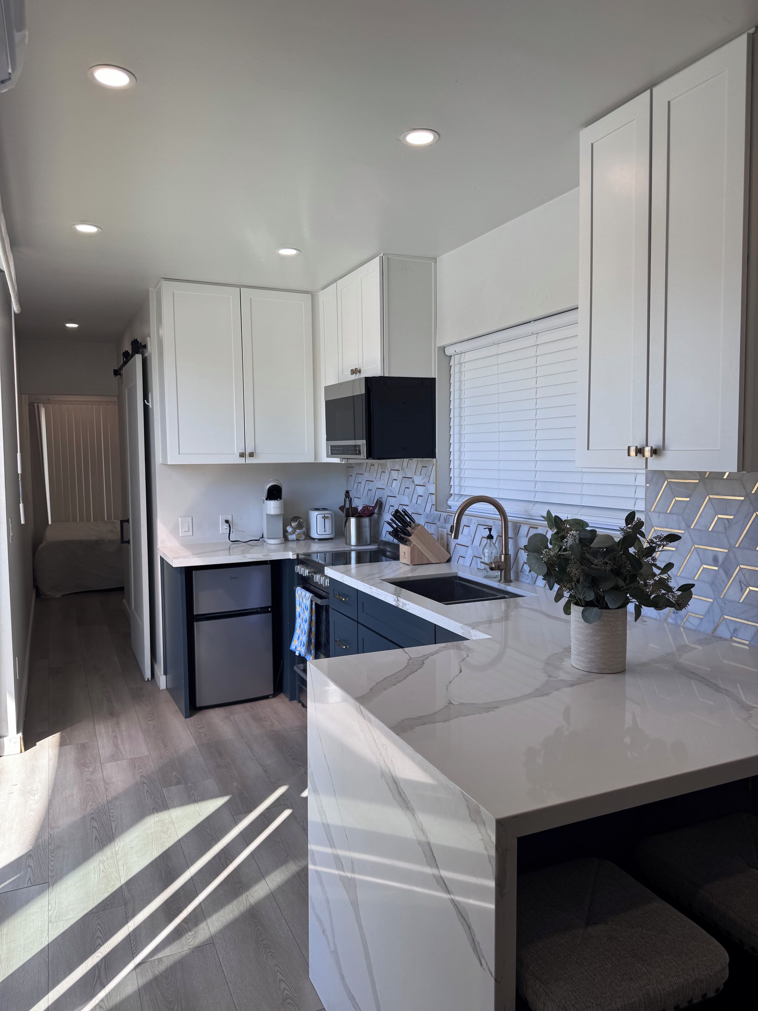 A modern kitchen with white cabinets, a marble countertop, and a built-in oven.