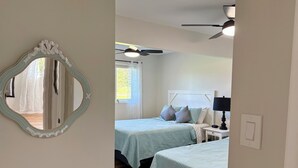A bedroom with two beds, a ceiling fan, a bedside table with a lamp, and a mirror on the wall. - Riverside Landing Cottage (Alberton)