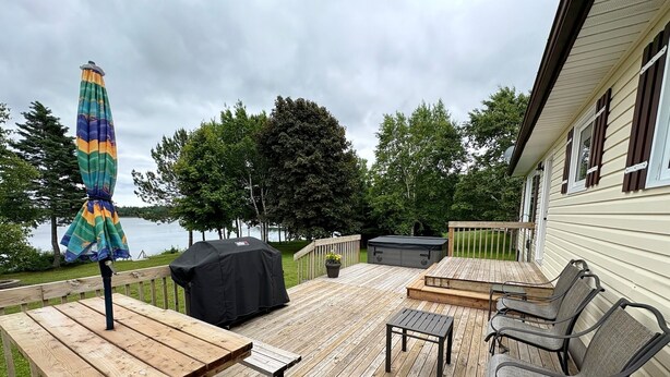 A wooden deck with a table and chairs, a grill, and a covered umbrella. - Riverside Landing Cottage (Alberton)