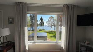 A room with a large window, a bed, a TV, and a small table with a lamp. - Riverside Landing Cottage (Alberton)