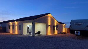 A single-story building with a covered patio area, a visible garage door, and a large RV parked adjacent to it.