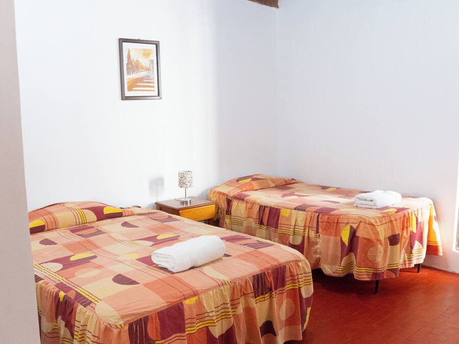Una habitación con dos camas, cada una con colcha estampada, una mesita de noche con lámpara y un cuadro en la pared.