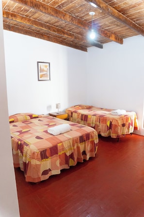 A room with two beds, each covered with patterned bedspreads, a small bedside table with a lamp, and a framed picture on the wall.