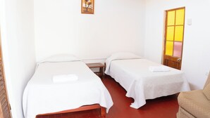 A room with two single beds, a wooden chair, a small table, and a window with a wooden frame. - Hawka (Ica)