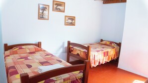 A room with two wooden beds, each with a patterned bedspread. There are three framed pictures on the wall. - Hawka (Ica)