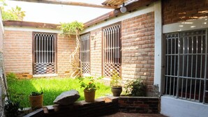A brick building with barred windows and a small garden area with potted plants. - Hawka (Ica)