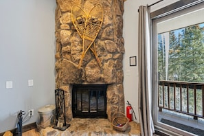 A stone fireplace with a decorative piece above it, a fire extinguisher, and a window with a view of trees.