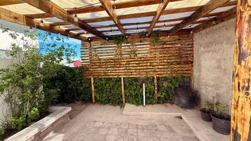 Un área de patio techada con una pérgola de madera, plantas en macetas y piso de concreto.