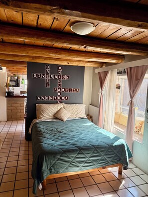 Cozy bedroom with a large bed, wall-mounted crossword puzzle, and a small kitchen area.