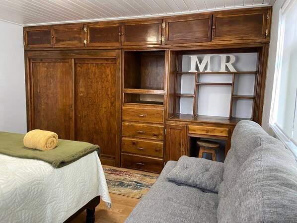 A bedroom with a bed, a wooden wardrobe, a desk with drawers, and a grey sofa.