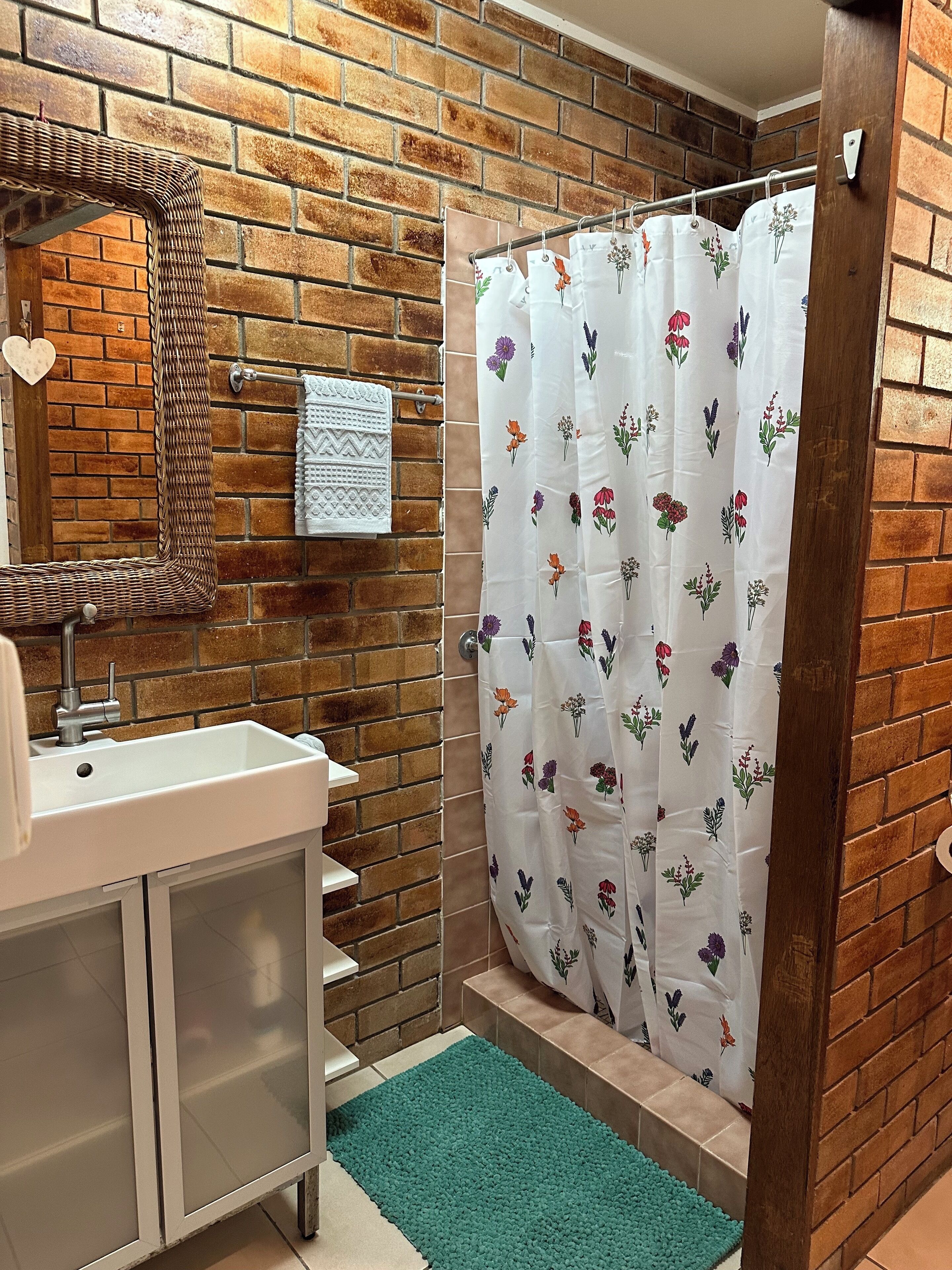 A bathroom with a white sink, a mirror, a towel rack with a white towel, a shower curtain with floral patterns, and a green rug.