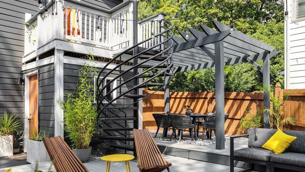 A patio with a wooden deck, a gray outdoor sofa with a yellow pillow, a wooden chair, a small round table, and a spiral staircase leading to a balcony. - Colorful private guesthouse in charming Richmond with Parking (Richmond)