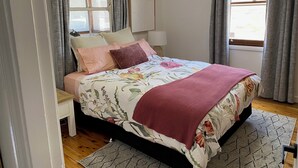 A bedroom with a bed, a nightstand, a lamp, a window, and a view of the outside. - The Merchant's Nook (Armidale)