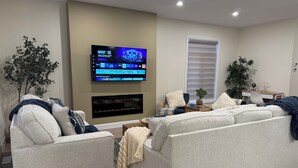 Uma sala de estar moderna com televisão de tela plana na parede, lareira abaixo e área de estar confortável com sofá e poltronas.